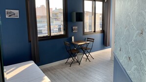 Una habitación con cama, una mesa pequeña con sillas, una ventana y un televisor de pared.