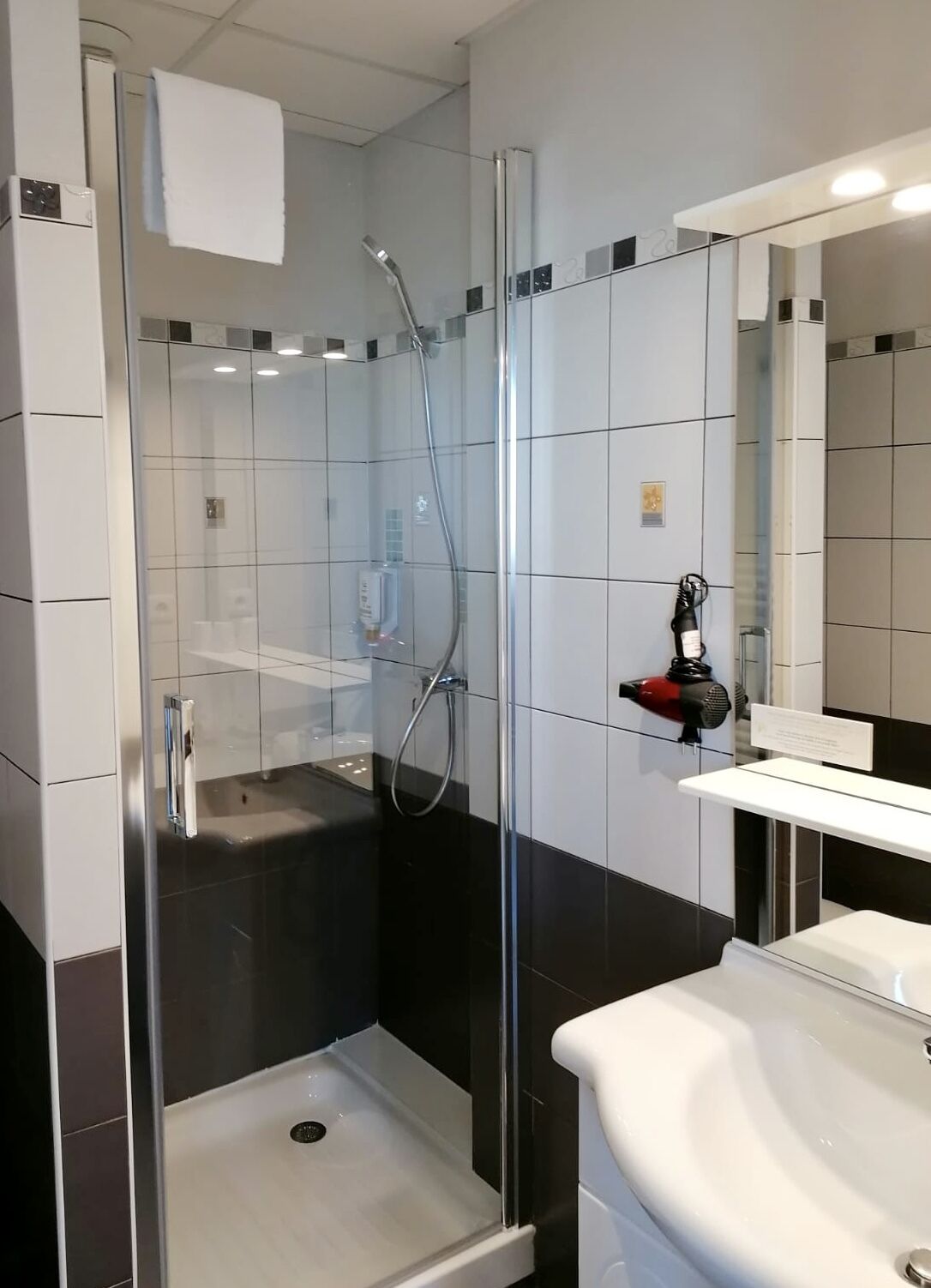 Un baño moderno con ducha envuelta en vidrio, un lavamanos blanco y un espejo.