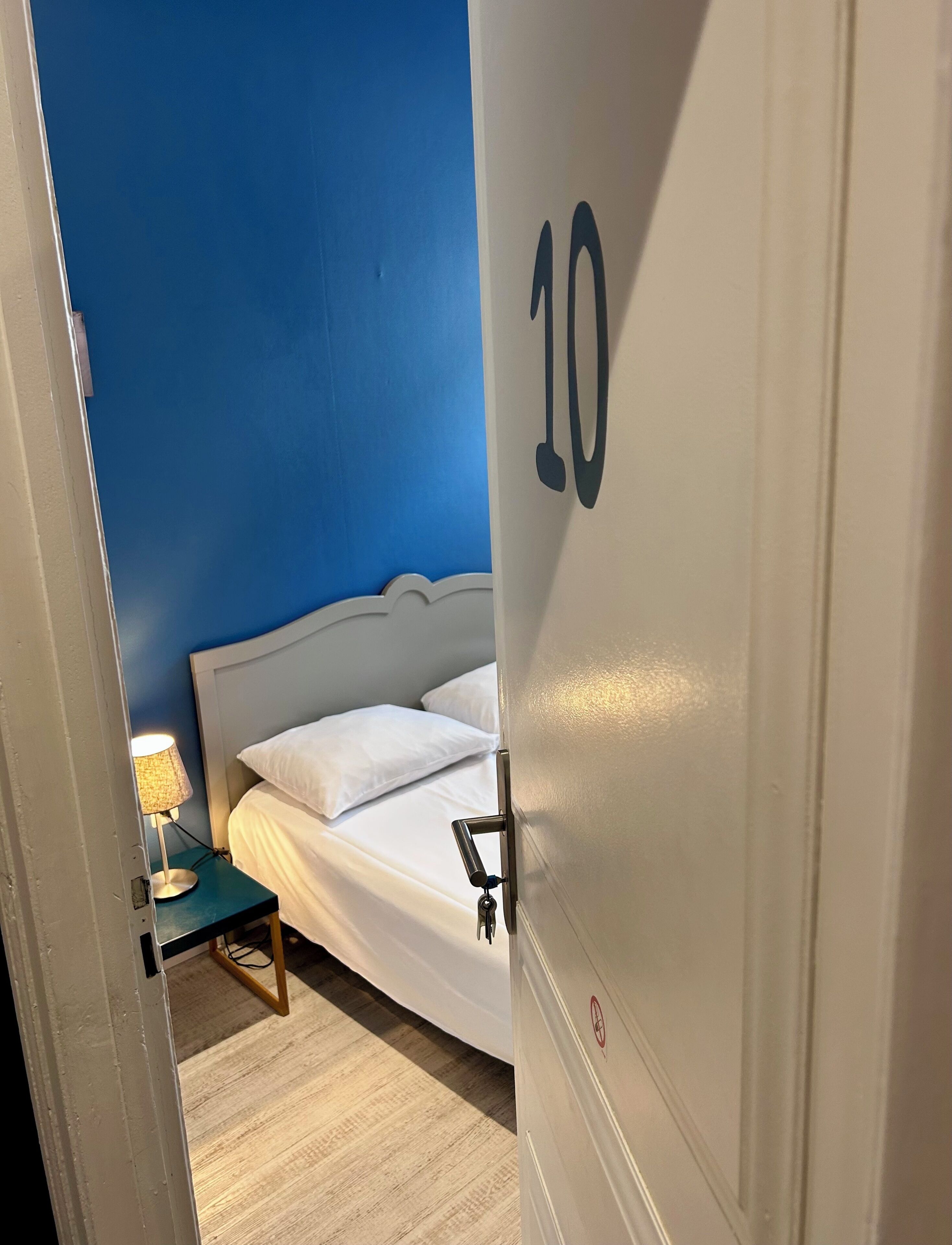 Una habitación de hotel con una cama, una mesita de noche con lámpara y una puerta con el número 10.