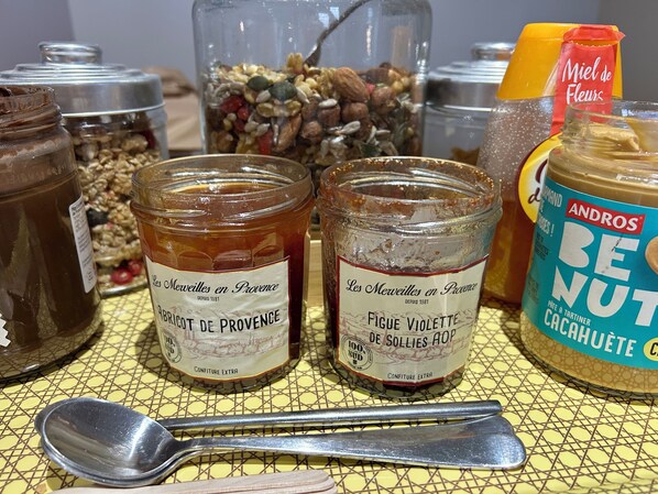 Three jars of Provençal preserves on a yellow tablecloth with a spoon and a bottle of orange juice.