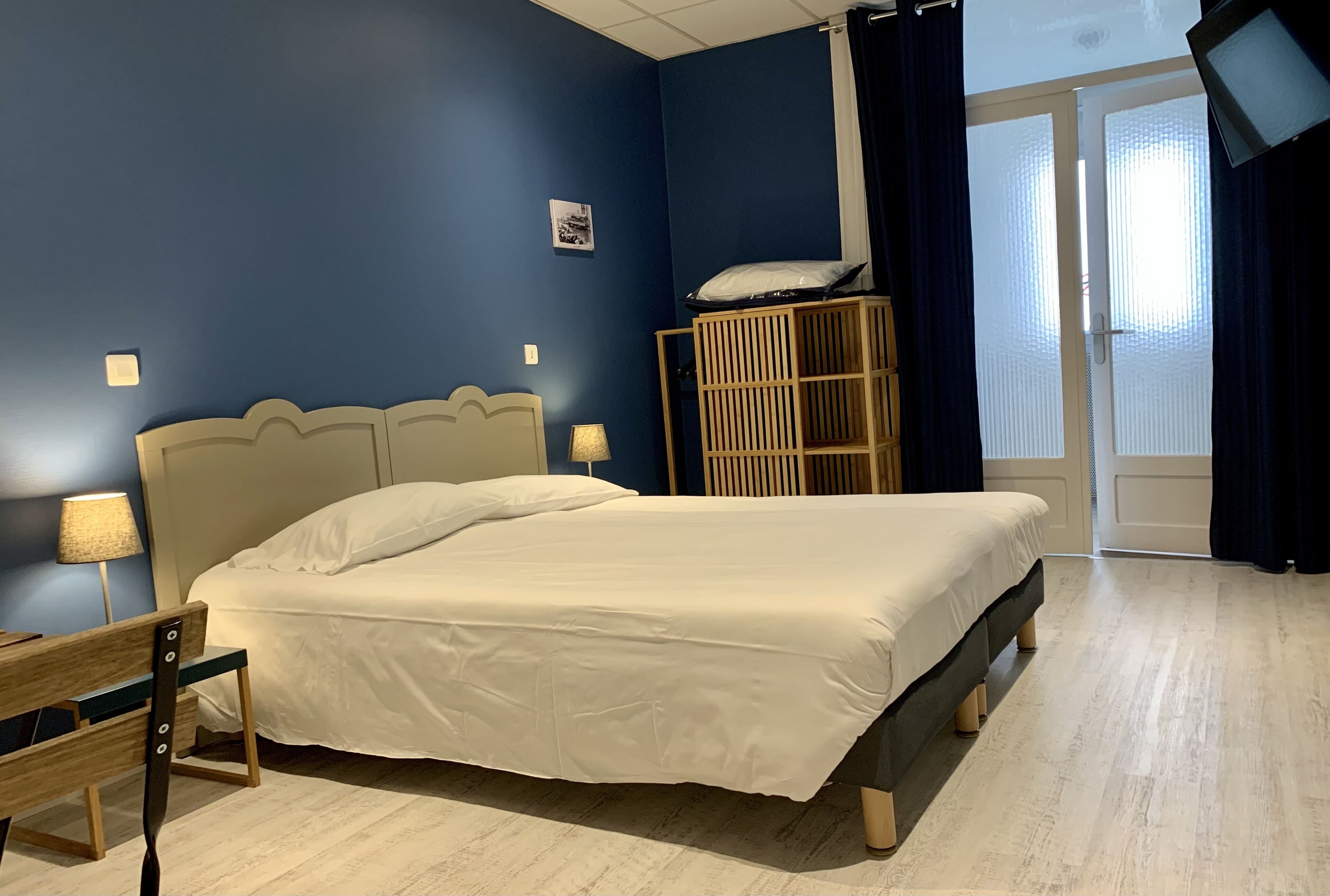 Une chambre à coucher avec un lit, un banc en bois, une table de chevet avec une lampe, un berceau et un téléviseur fixé au mur.