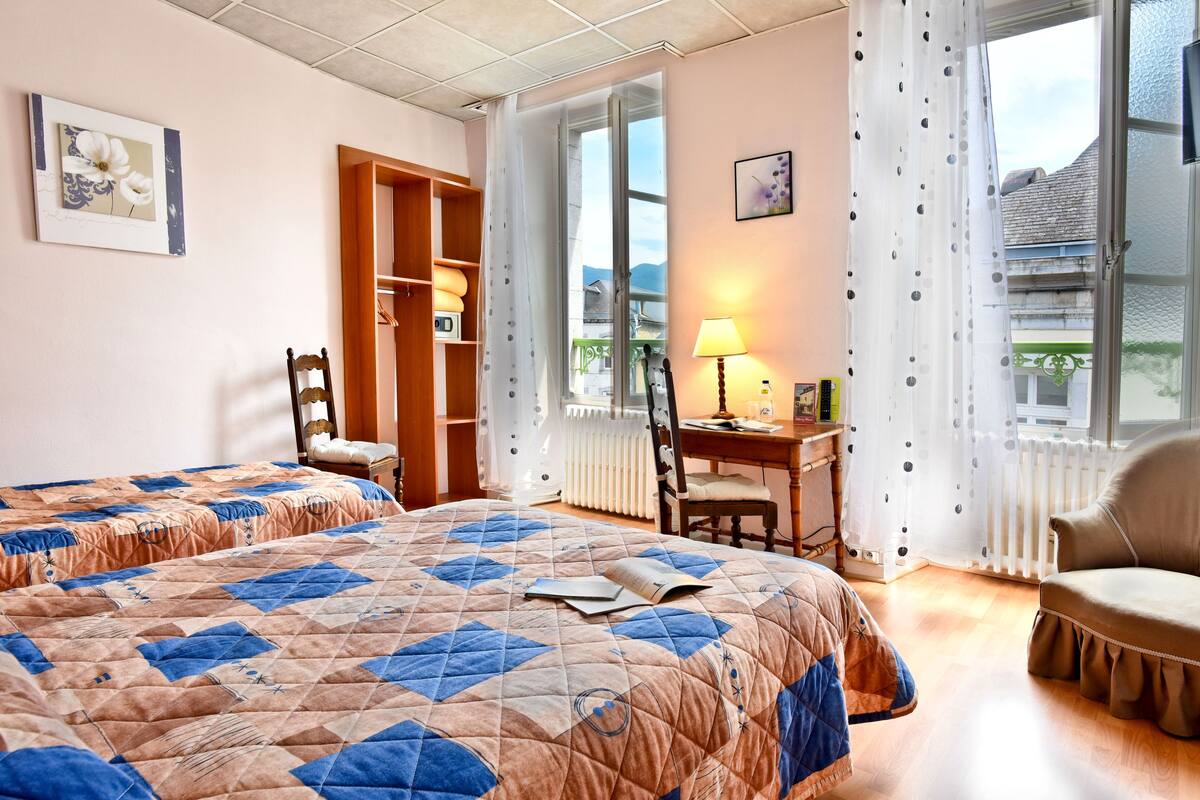 A bedroom with two beds, a desk, a chair, and a window with curtains.