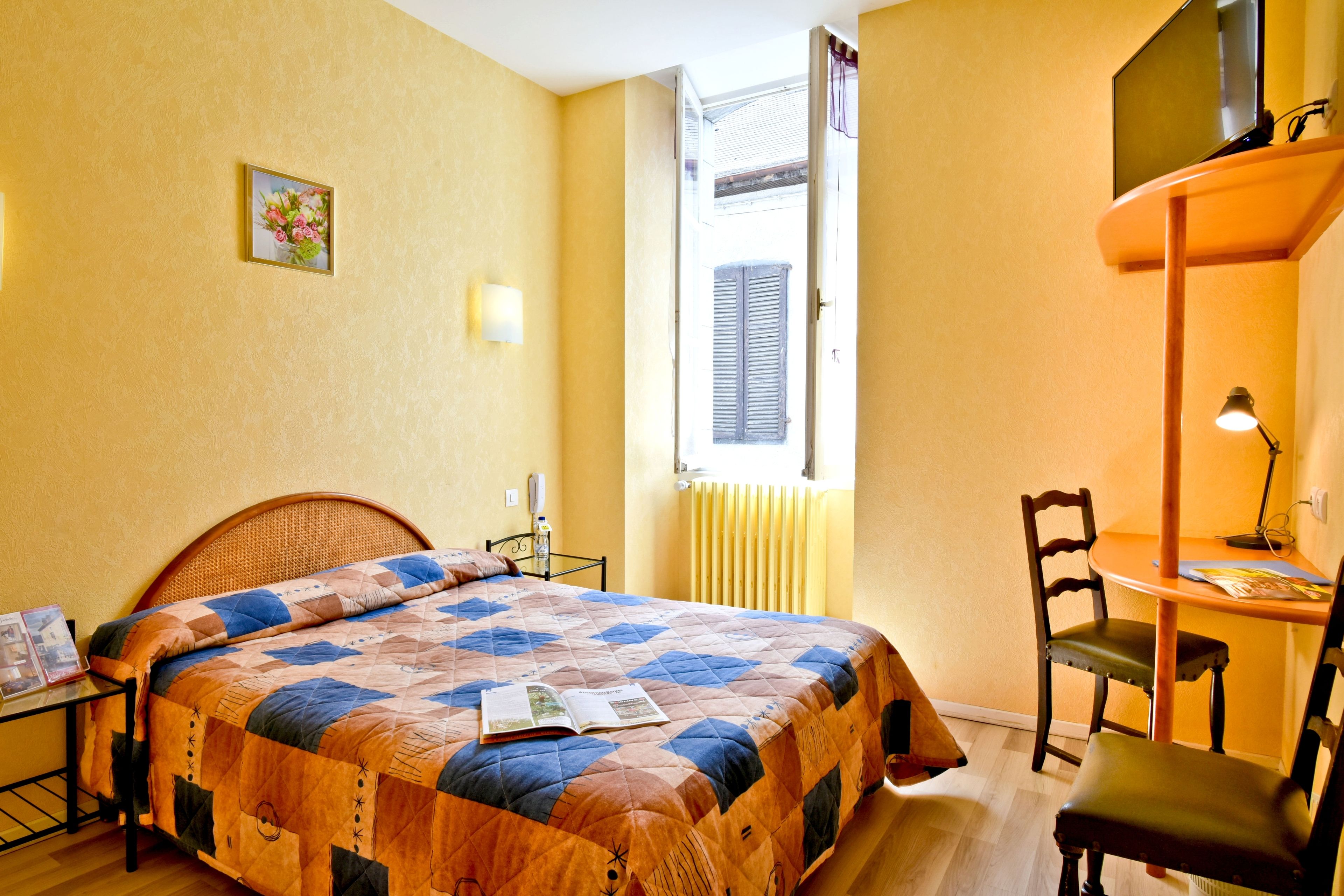 A bedroom with a bed, a desk, a chair, a window, and a radiator.