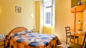 A bedroom with a bed, a desk, a chair, a window, and a radiator.