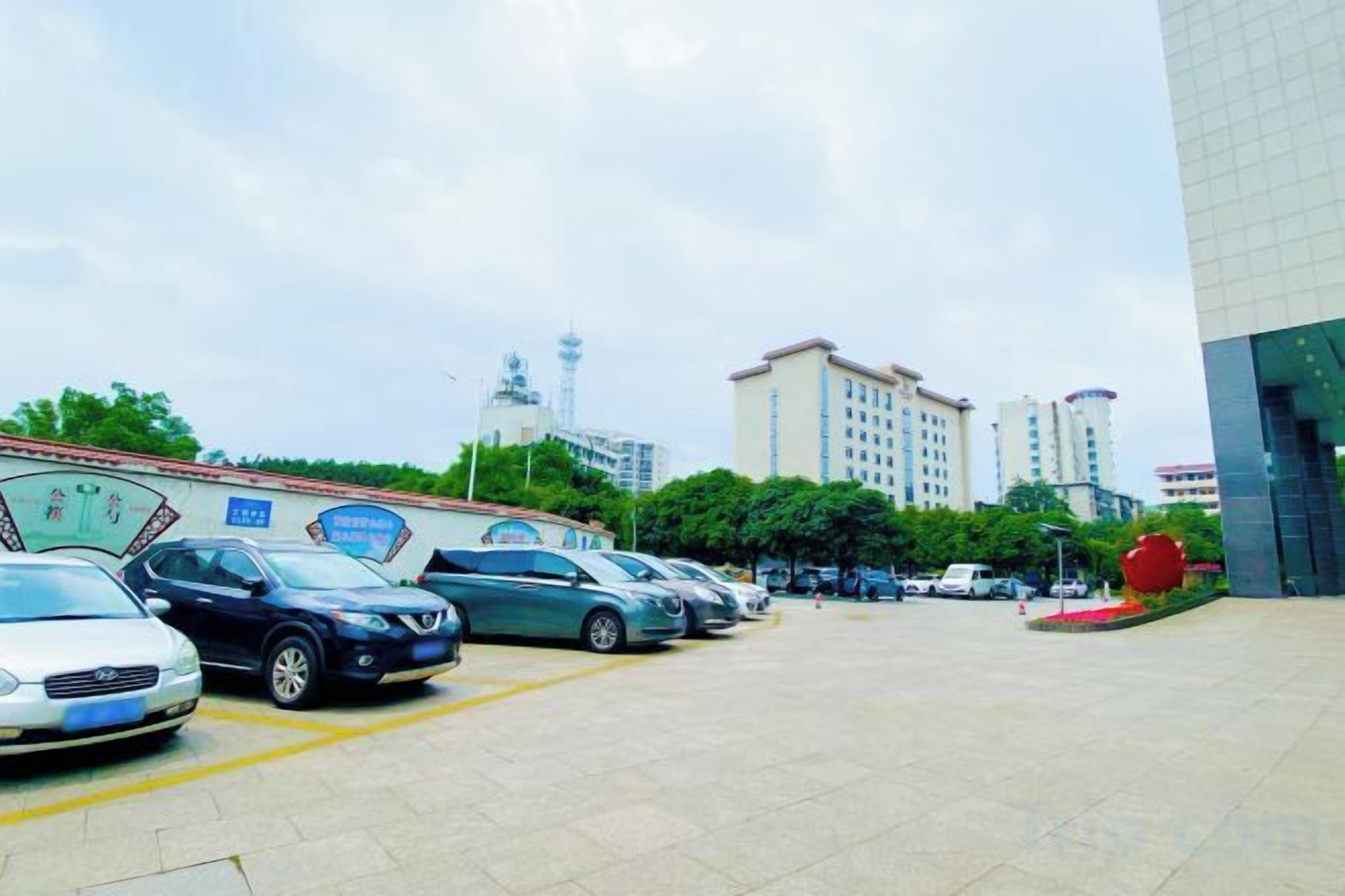 Un estacionamiento con coches, un edificio de fachada moderna y una torre al fondo.