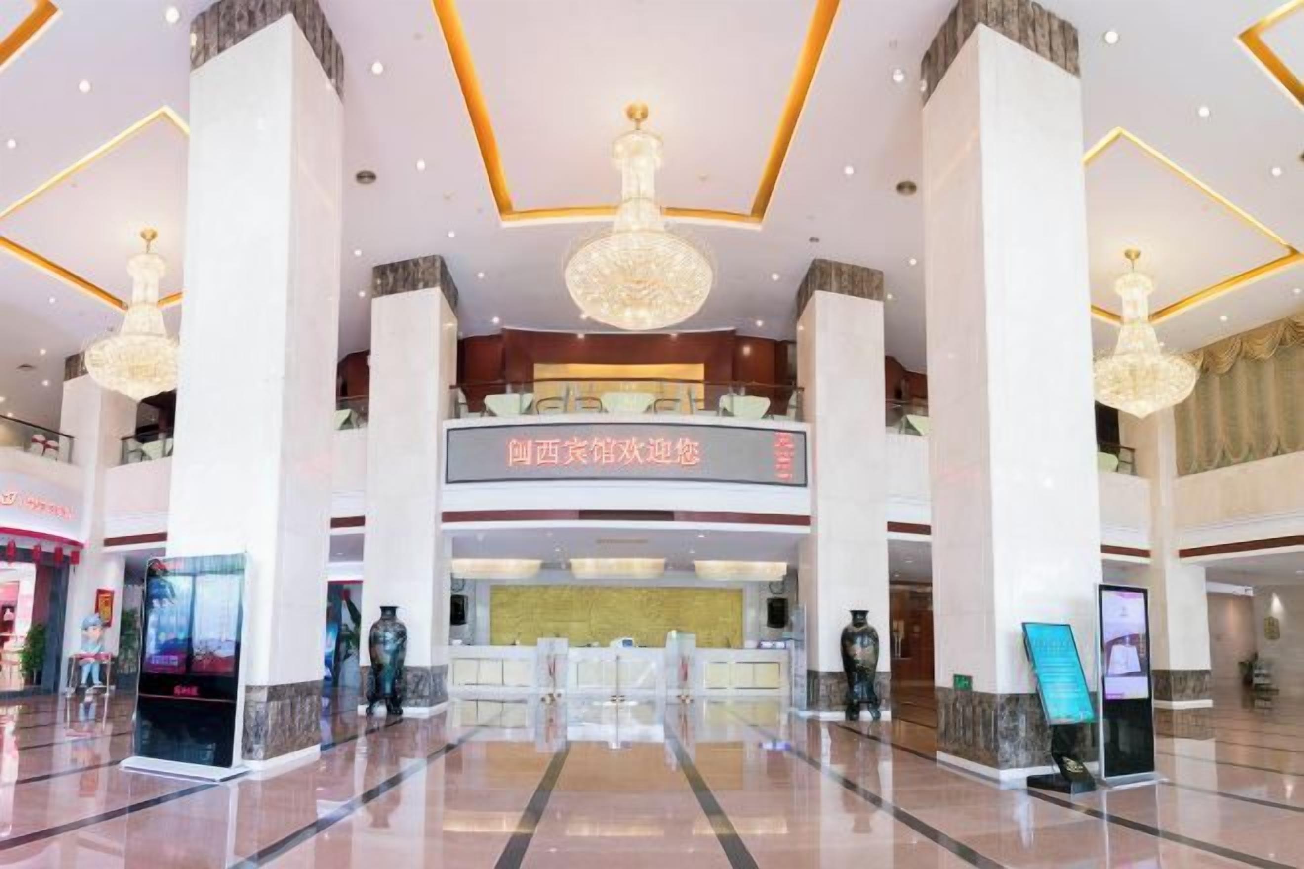 A spacious lobby with a reception desk, chandeliers, and a digital information kiosk.