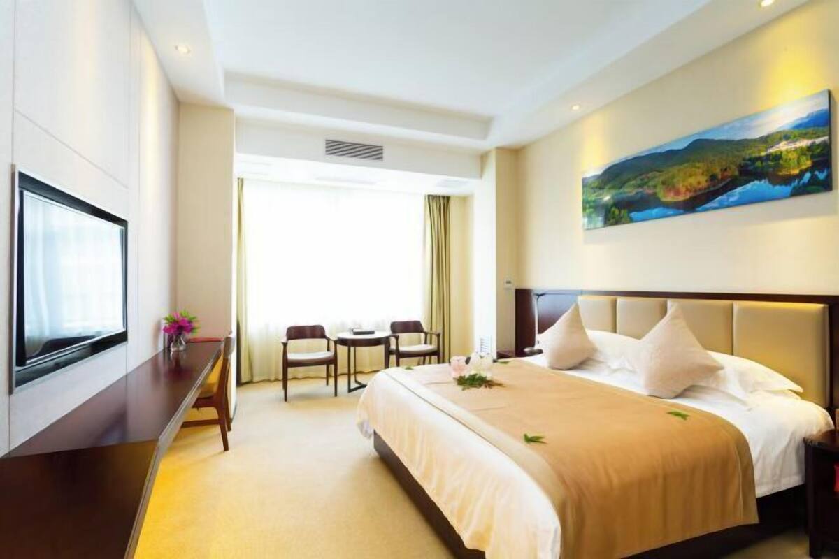 A hotel room with a bed, a desk, a TV, and a painting on the wall.
