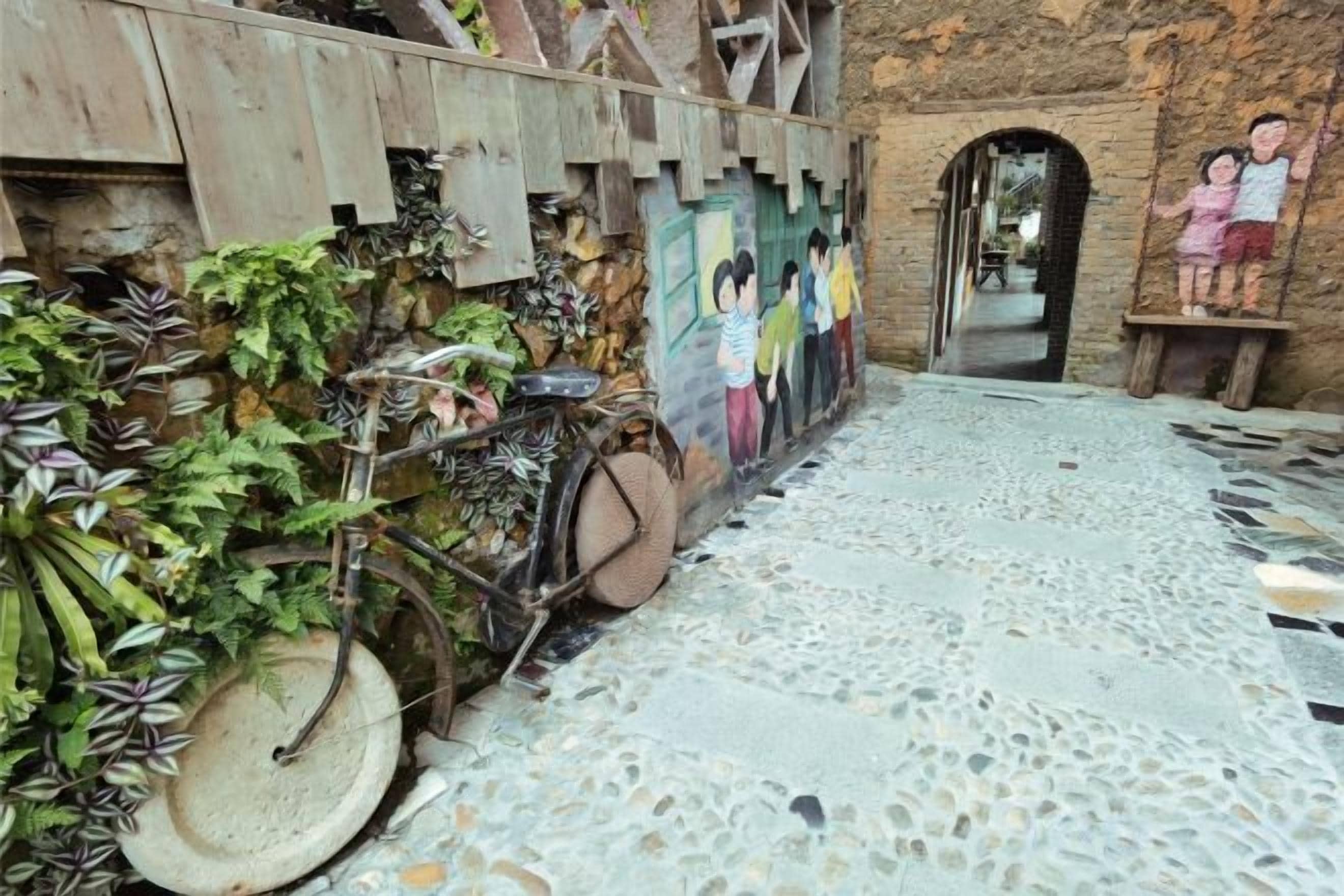 Une cour intérieure avec un vélo, des plantes et une fresque murale.