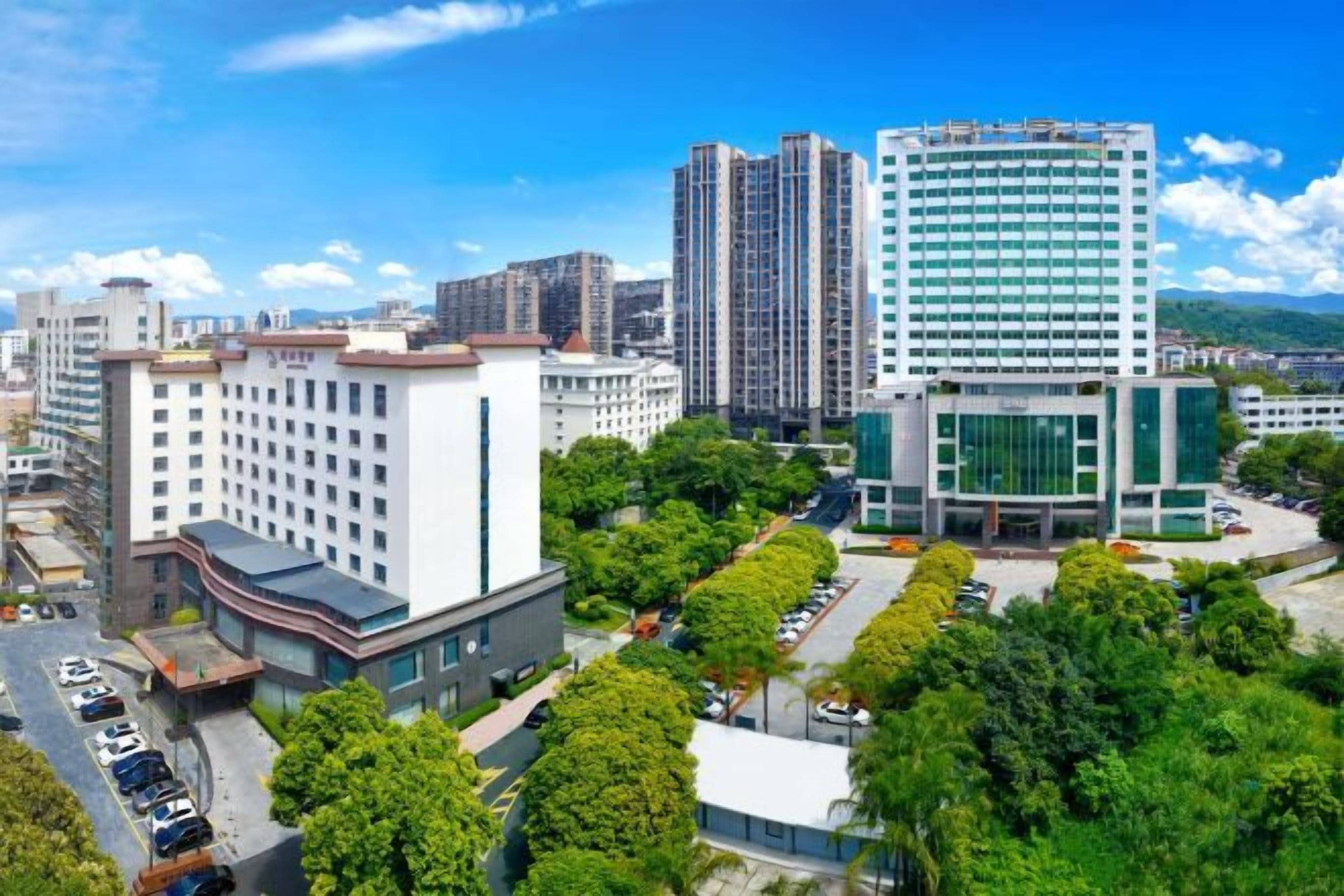 A modern building with a flat roof, surrounded by greenery and other buildings.