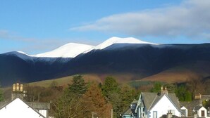 A mountain with a snow-capped peak, a town with houses, and a clear sky. - Salisbury Guest House (Keswick)