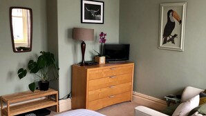 A bedroom with a bed, a wooden dresser, a TV, a mirror, and a framed picture on the wall. - Salisbury Guest House (Keswick)