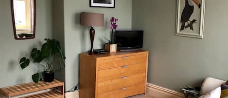 Un dormitorio con una cama, un aparador de madera, un televisor, un espejo y un cuadro en la pared.