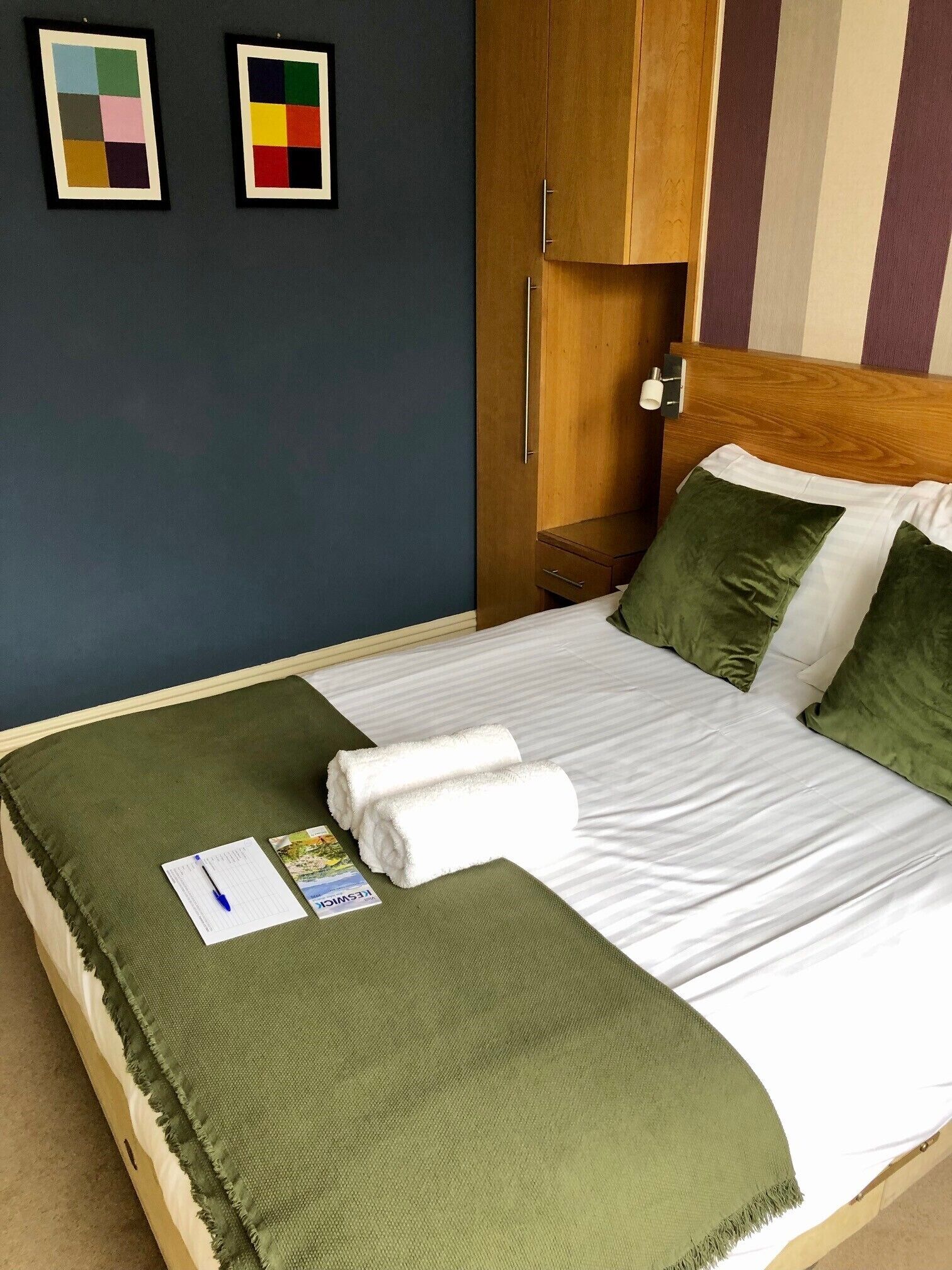 A neatly made bed with green bedding, a wooden wardrobe, and two framed color charts on the wall.
