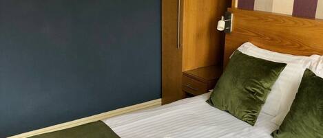 A neatly made bed with green bedding, a wooden wardrobe, and two framed color charts on the wall.