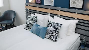 A neatly made bed with white and patterned pillows, a grey upholstered chair, and wall art.