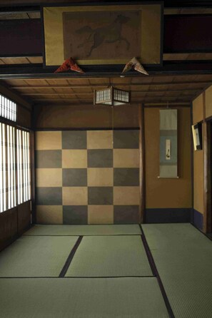 Une pièce traditionnelle avec un sol recouvert de tatamis, un mur à carreaux, un tableau encadré et une porte coulissante.