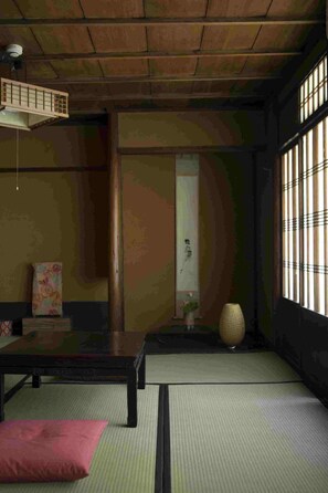 Um quarto japonês tradicional com tatames, uma mesa de madeira baixa, um banco acolchoado e uma porta de papel shoji.