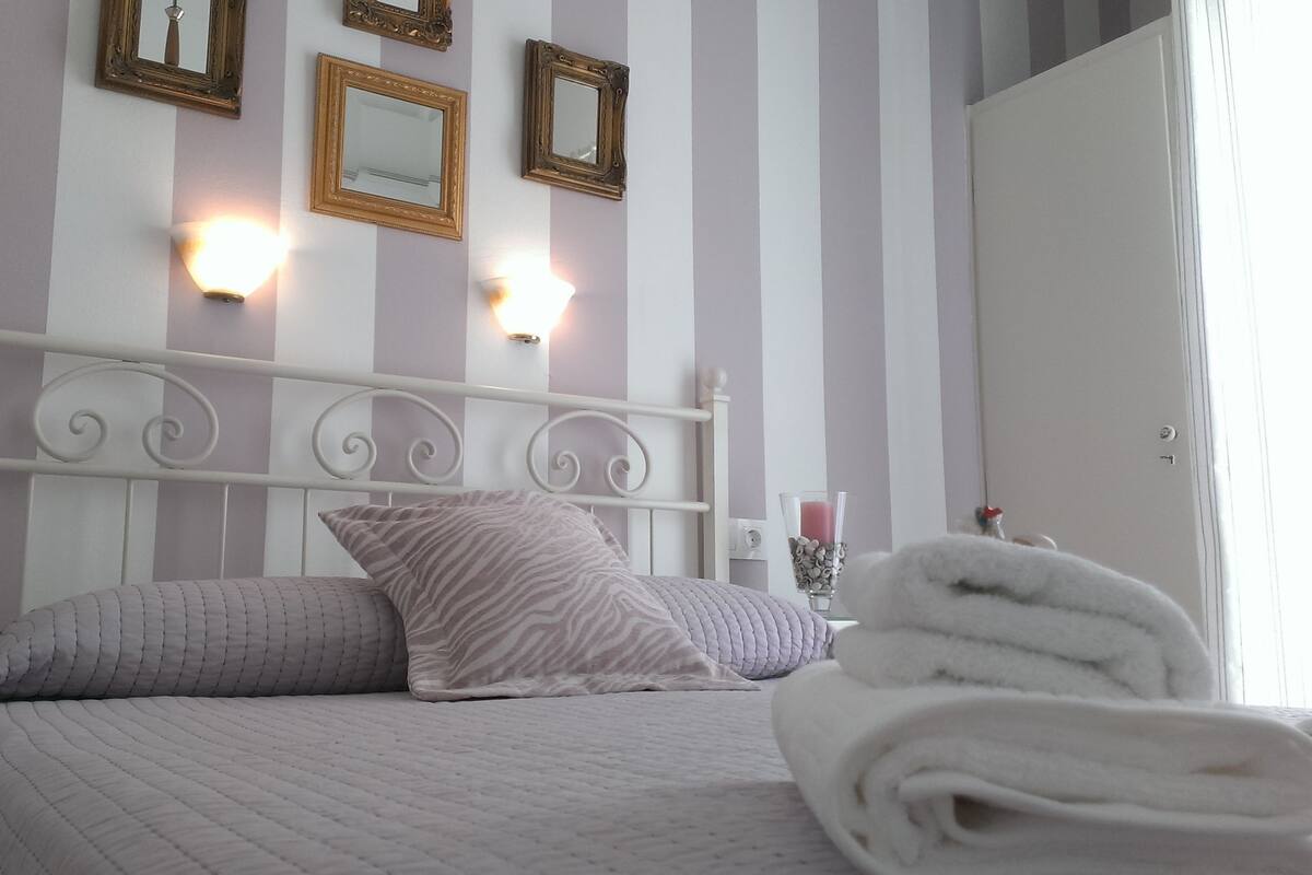 A neatly made bed with striped bedding, a headboard with decorative scrollwork, and wall-mounted mirrors.