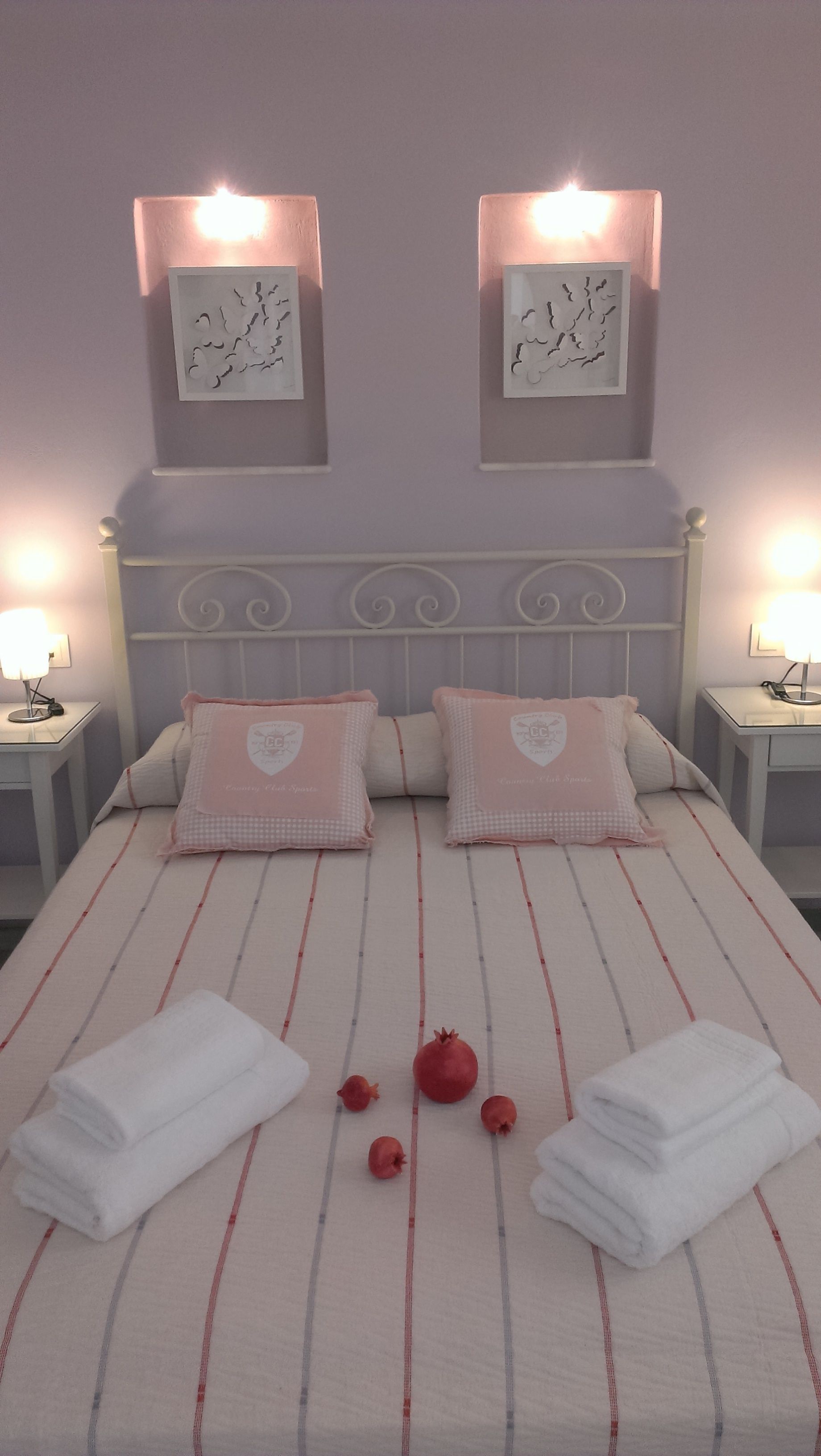 Een tweepersoonsbed met gestreept beddengoed, twee nachtkastjes met lampen en twee aan de muur bevestigde fotolijstjes.