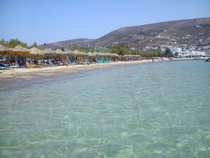 Una playa con agua cristalina, sombrillas y sillas.