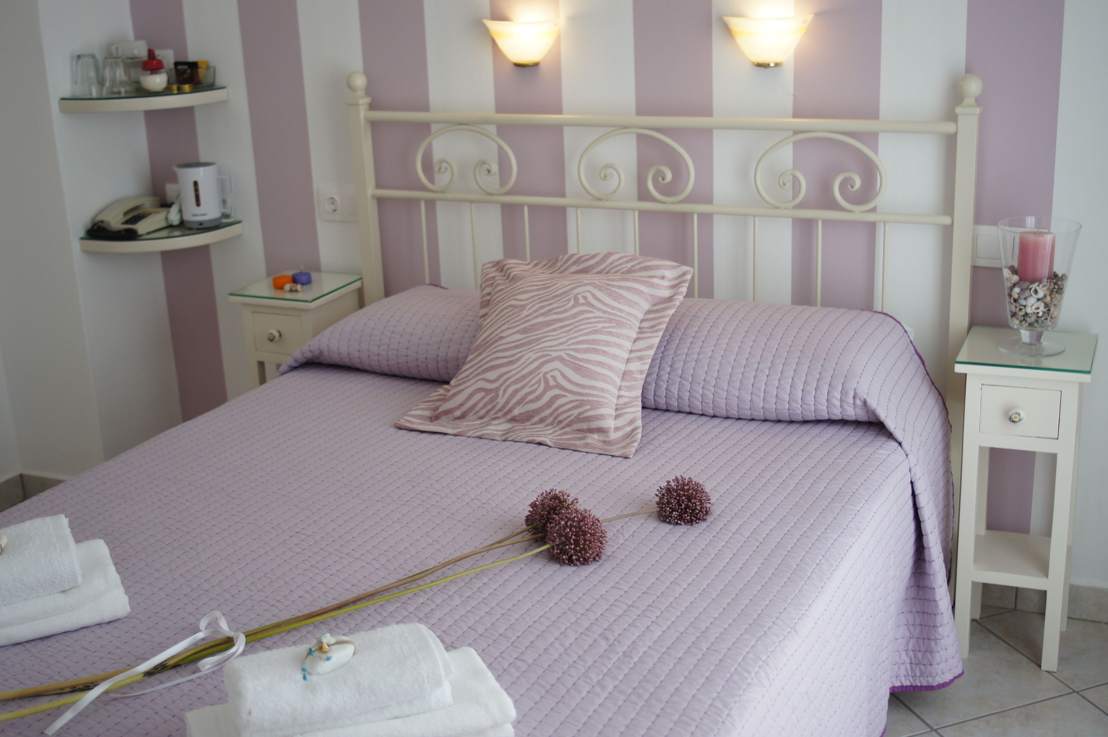 Een net opgemaakt bed met een paarse quilt, een kussen met luipaardprint en decoratieve bloemen.