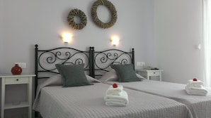 A double bed with two pillows, a bedside table with a lamp, and a wall-mounted light fixture. - Cyclades Hotel (Paros)