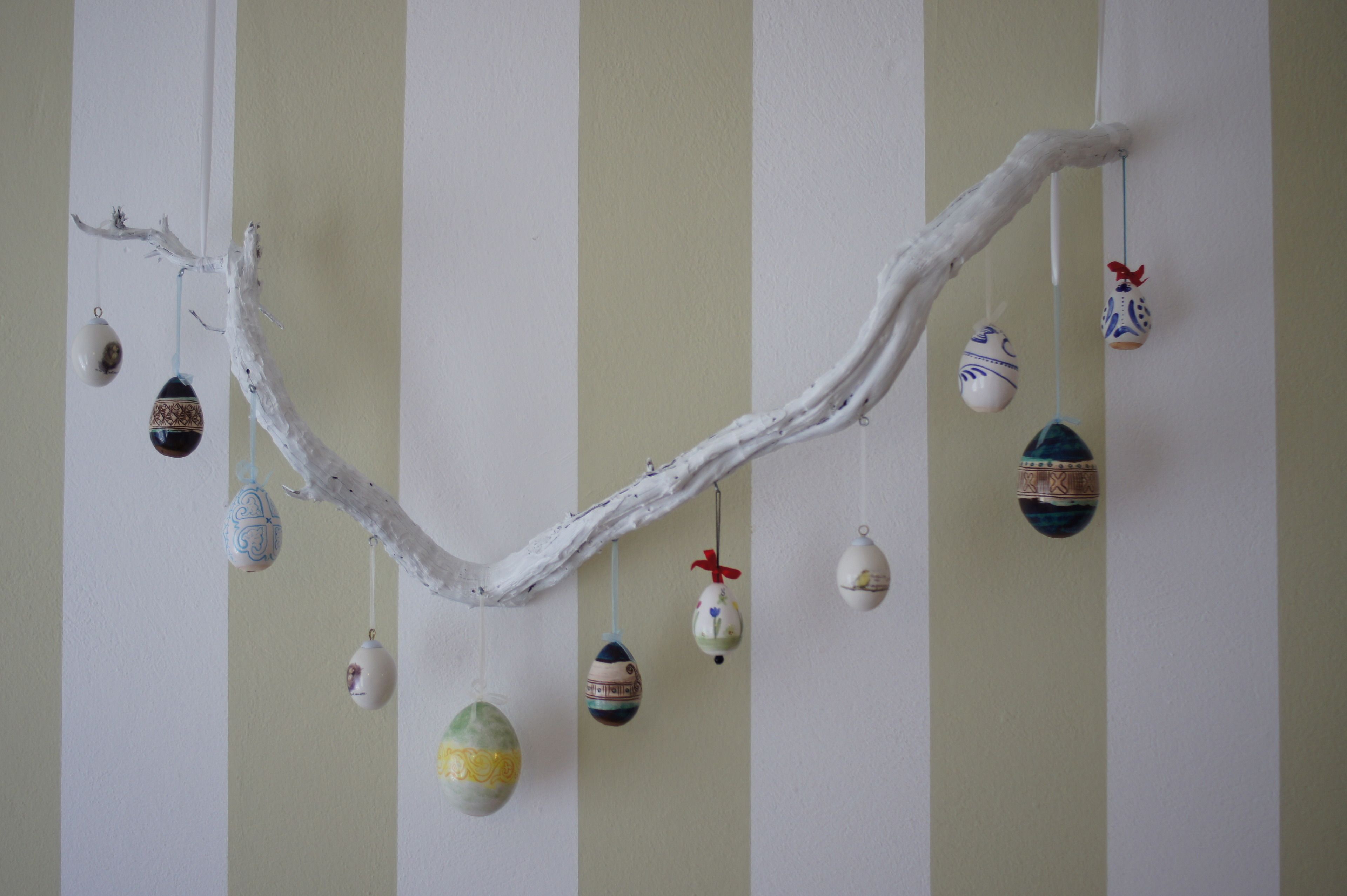 A branch with hanging ornaments against a striped wall.