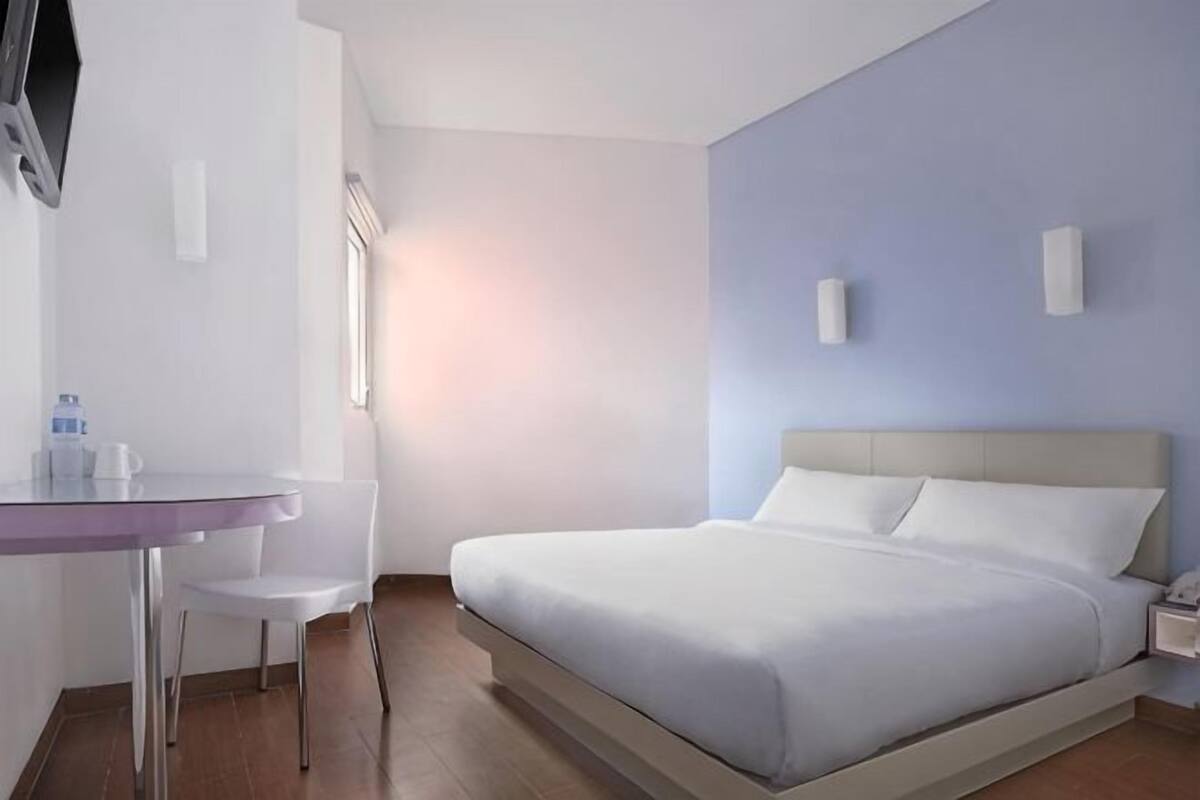 A hotel room with a bed, a desk, a chair, and a TV.
