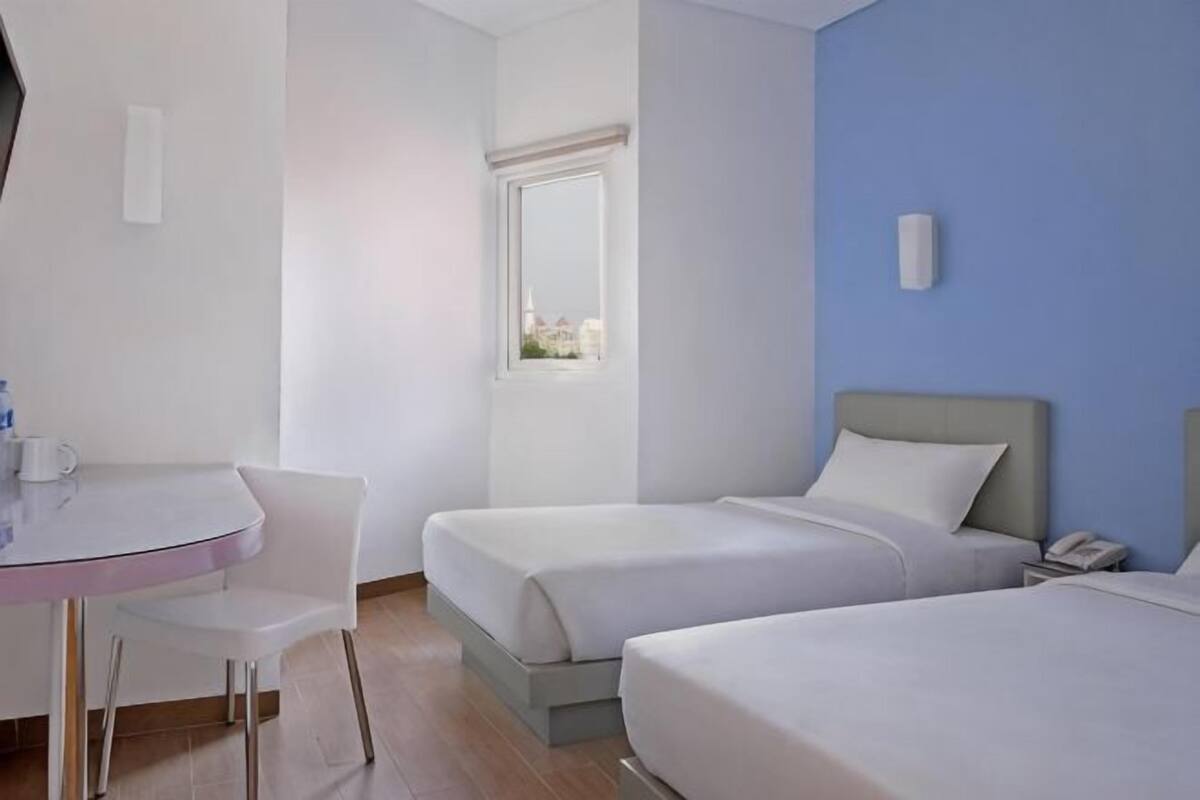 A hotel room with two beds, a desk, and a chair.