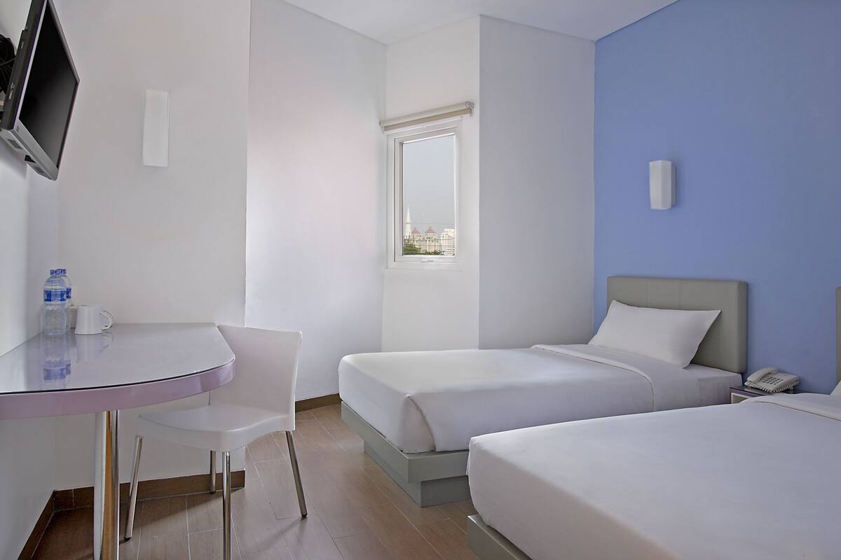 A hotel room with two beds, a desk with a chair, a TV, a window with a view, and a phone on the bedside table.