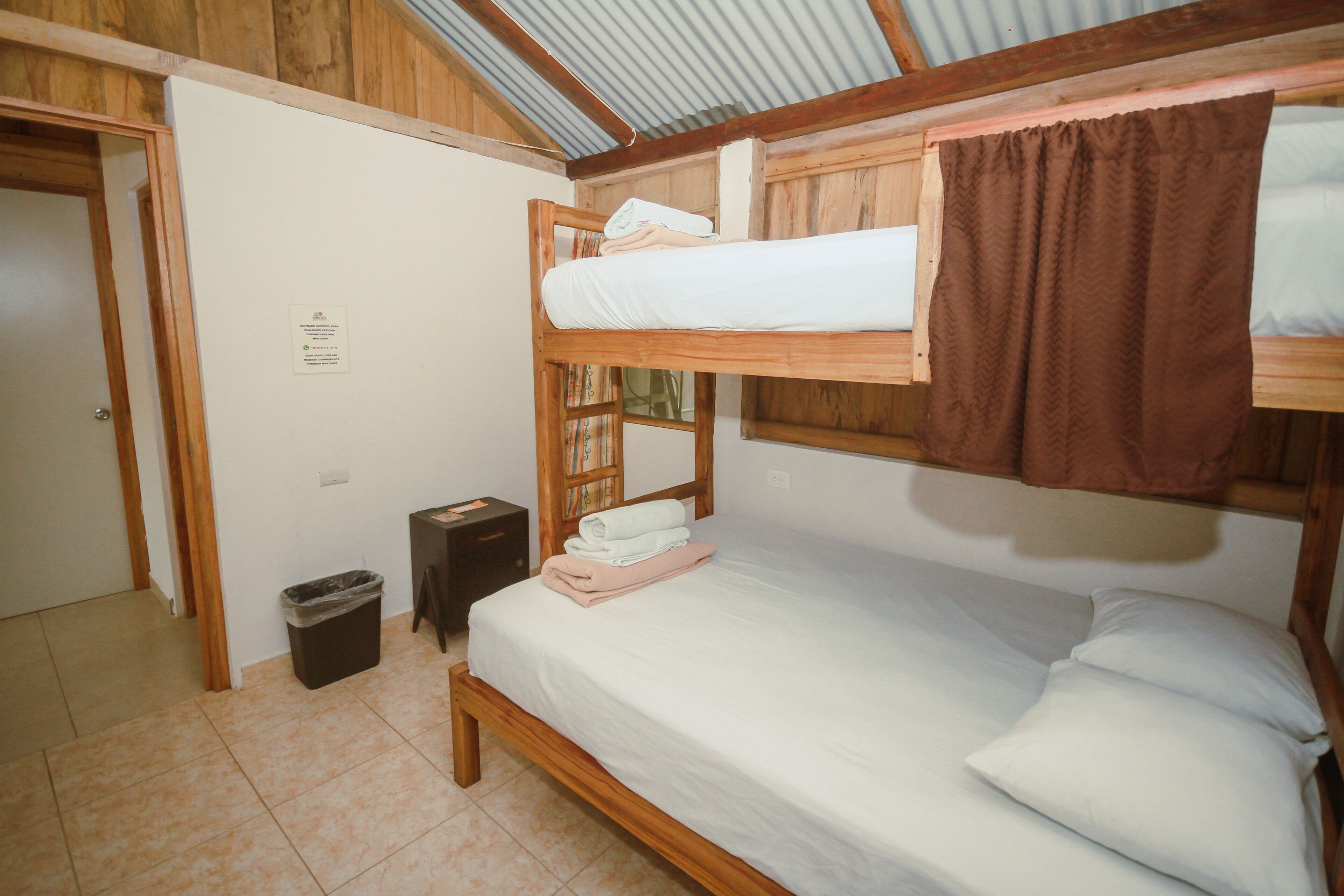 Habitación con literas, techo de madera, un cubo de basura y una puerta.