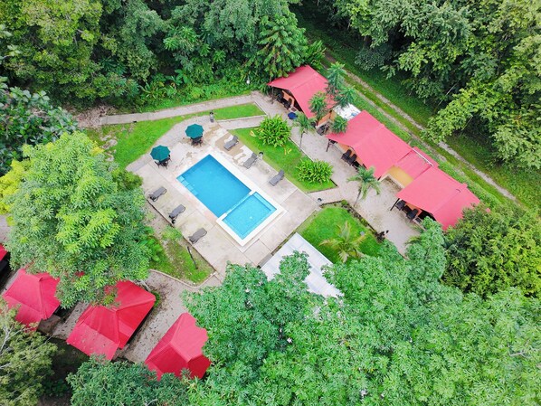 An aerial view of a resort with a swimming pool, lounge chairs, and red-roofed structures.