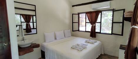 Un dormitorio con cama, lavamanos y ventana con cortinas.