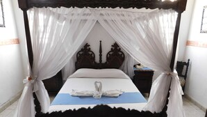 Una cama con dosel, con un edredón azul y una toalla dispuesta en forma de corazón sobre la cama.