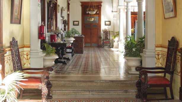 Un amplio pasillo con columnas ornamentadas, un suelo con diseño y mobiliario clásico.