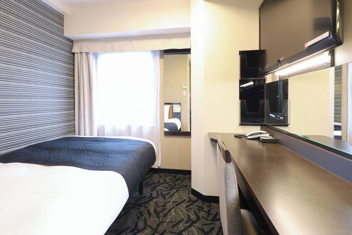 A hotel room with a large bed, a desk with a telephone, and a mirror.