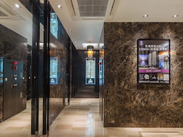 Un pasillo moderno de hotel con paredes de mármol, un directorio digital y un cartel promocional de un apartamento de dos dormitorios.