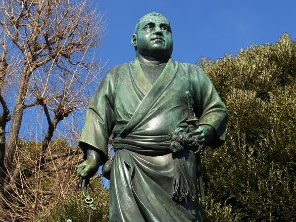 A statue of a historical figure in traditional attire, standing outdoors with trees and shrubs in the background. - APA Hotel Akihabara Ekimae (Tokyo)
