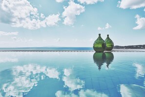 A clear pool with two green glass bottles on the edge, reflecting the sky and clouds. - Myconian Villa Collection - Preferred Hotels & Resorts (Mykonos)