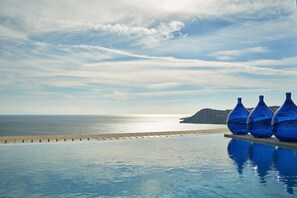 Una piscina con tres jarrones azules en el borde, con vista a una playa y el mar.