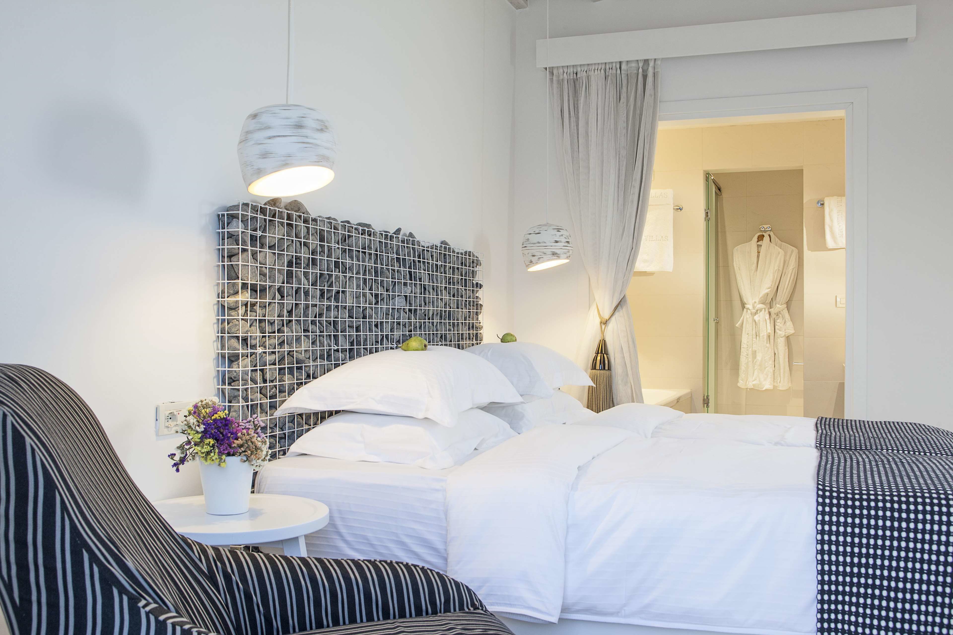 A modern hotel room with a neatly made bed, a small round table with a vase of flowers, and a unique wall decoration.