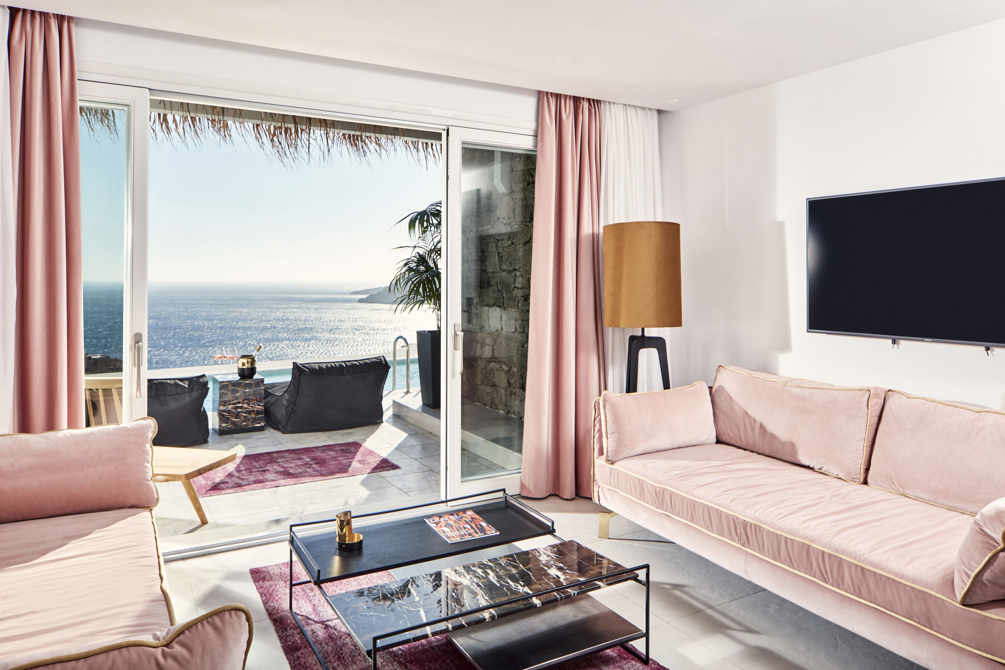 A modern living room with a large sliding glass door leading to a balcony with a view of the sea.