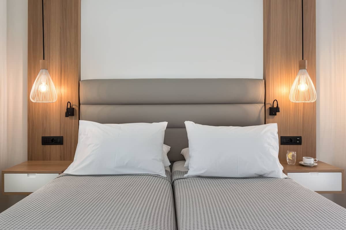 Una habitación de hotel moderna con una cama doble, dos mesitas de noche, una mesita de noche con lámpara y un panel de control en la pared.