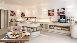 A modern breakfast buffet with a variety of food and drink options, a coffee station, and a seating area with a table set for breakfast. - Strogili Hotel - Adults Only (Santorini)