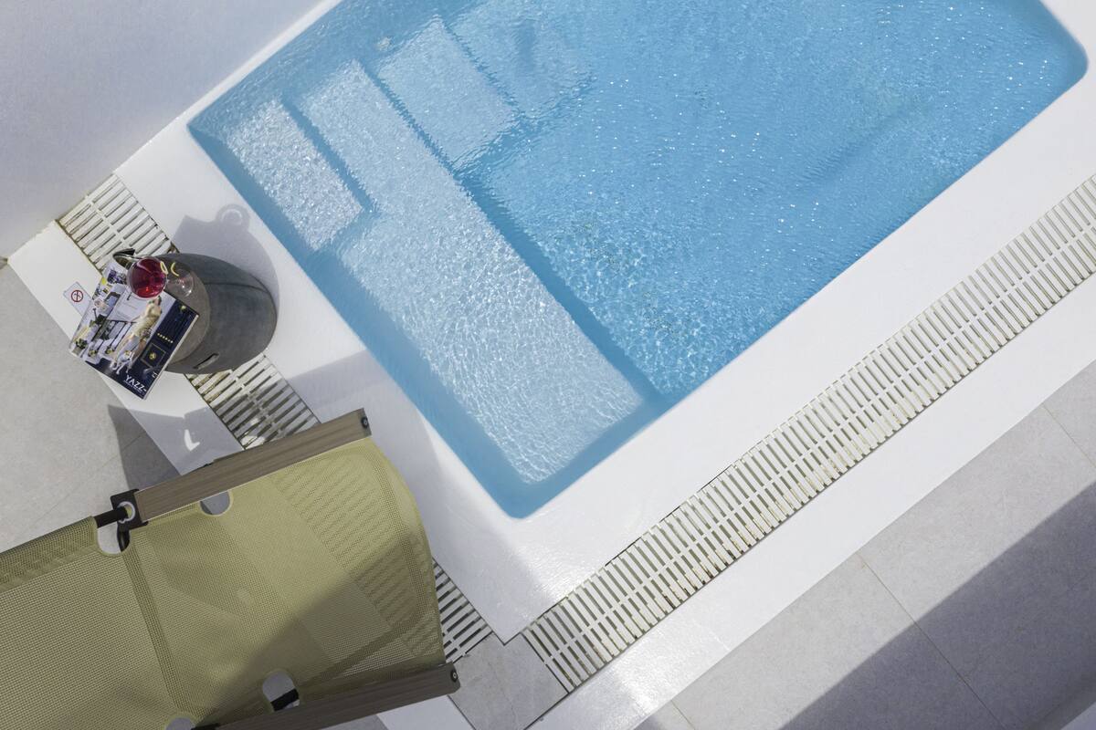 Zona de piscina con superficie de agua azul cristalina, una silla de descanso y una pequeña mesa con una bebida y un menú.