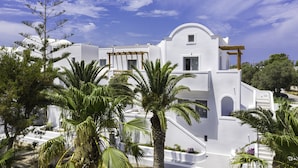 A white building with a curved roof, surrounded by palm trees and a clear sky. - Strogili Hotel - Adults Only (Santorini)