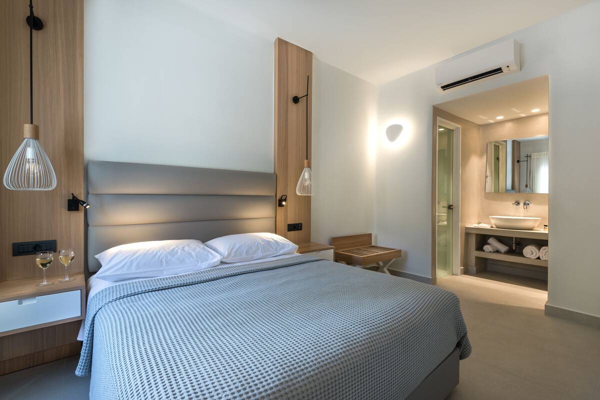 Un dormitorio moderno con una cama grande, mesitas de noche, un tocador, un espejo y un baño con lavamanos y toallero.