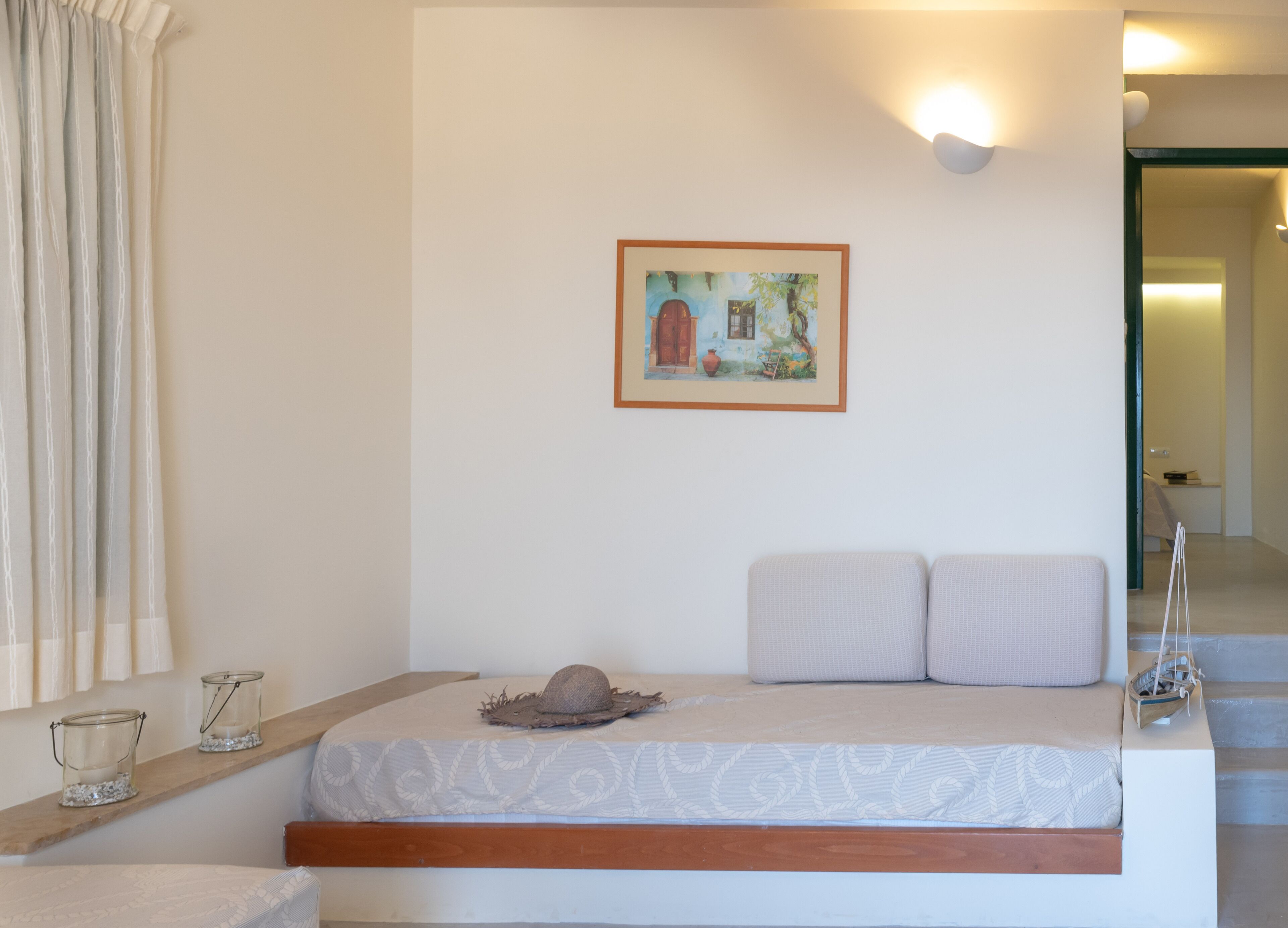 A bedroom with a bed, a headboard, a wall-mounted picture, a shelf with candles, and a window with curtains.