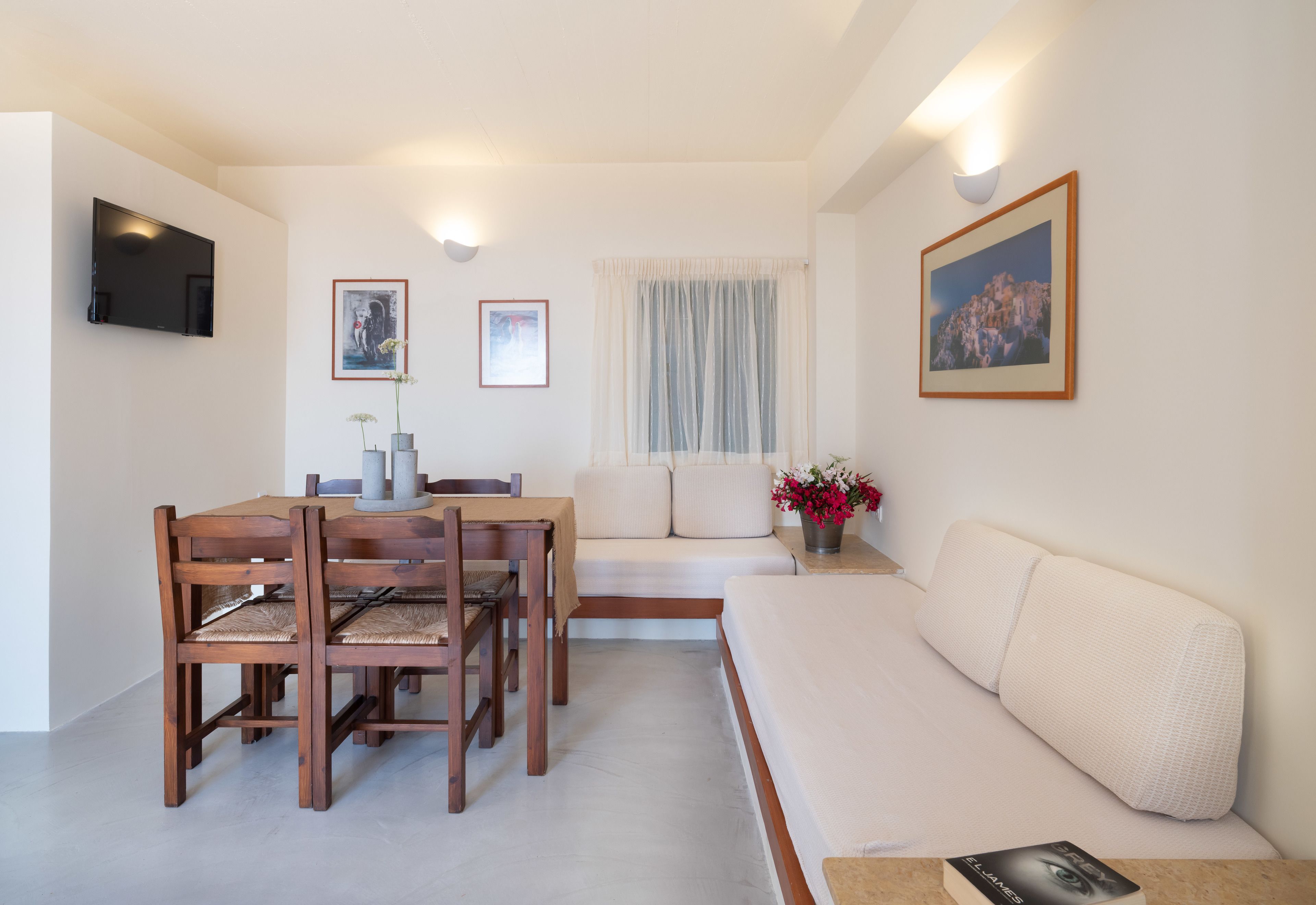A modern living room with a dining table, chairs, a sofa, and a television mounted on the wall.