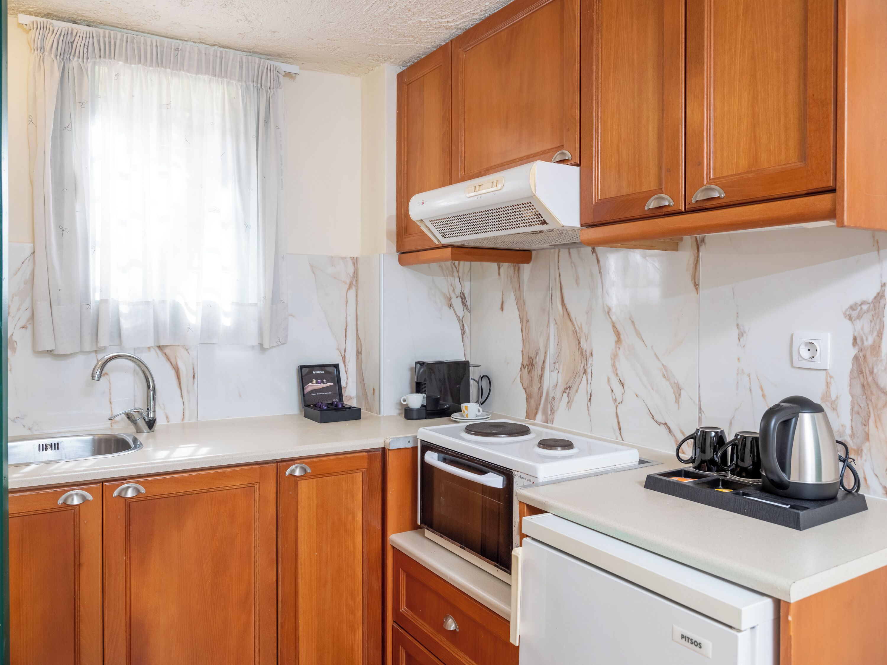 A compact kitchen with wooden cabinets, a built-in oven, a coffee maker, and a kettle on the countertop.
